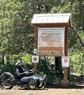 Man on adaptive bike looking up at Grindstone Trail System sign