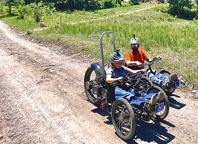 Two people riding adaptive bikes on a trail